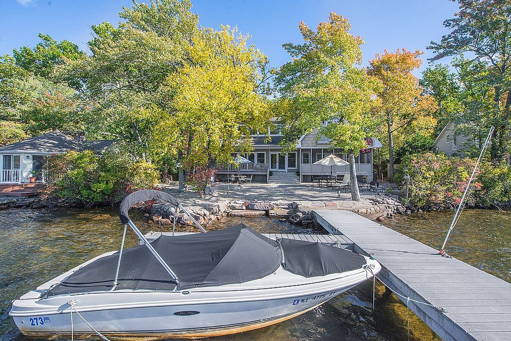 Speedboat docked by a wooden pier with a lakeside house surrounded by trees in the background.